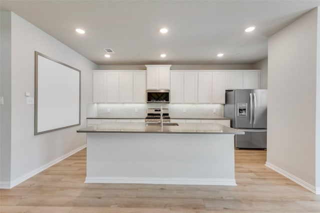 kitchen featuring white cabinets, an island with sink, appliances with stainless steel finishes, a sink, and backsplash