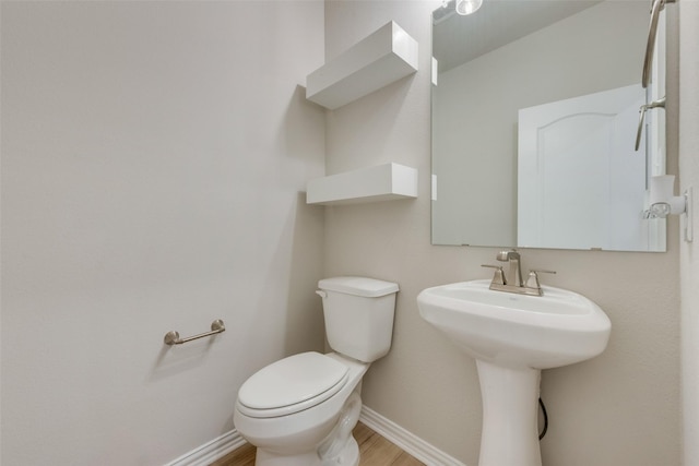 half bathroom featuring a sink, toilet, baseboards, and wood finished floors