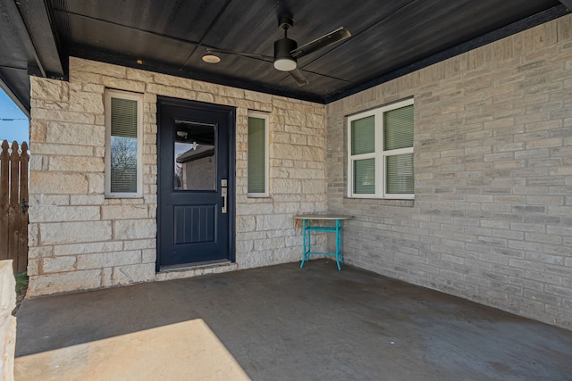 view of exterior entry with ceiling fan and brick siding