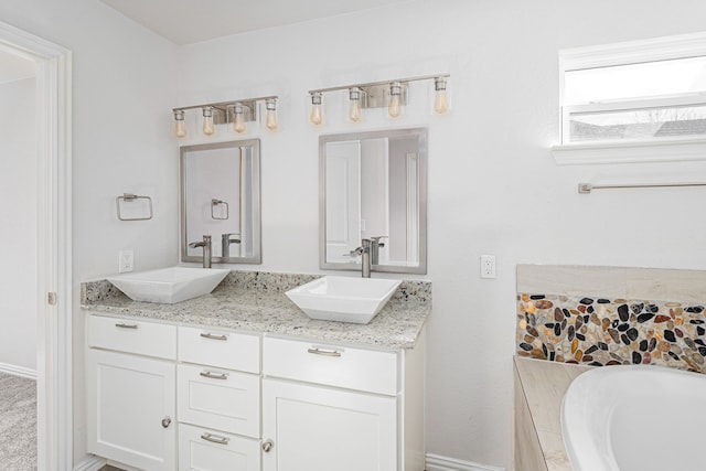 bathroom with double vanity, a tub to relax in, baseboards, and a sink