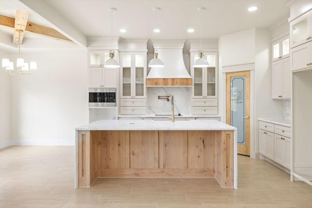 kitchen with an island with sink, custom range hood, light wood-type flooring, white cabinetry, and backsplash