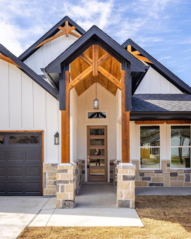 view of exterior entry featuring an attached garage, concrete driveway, stone siding, roof with shingles, and board and batten siding