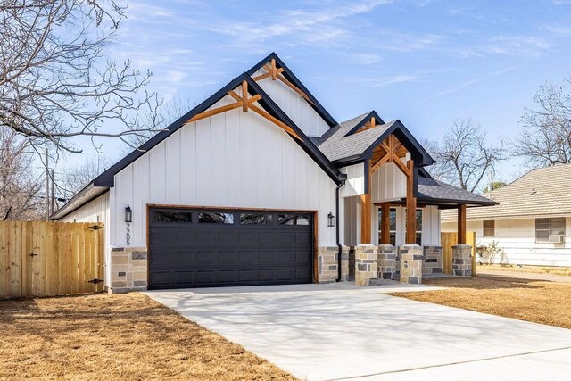 modern farmhouse style home with an attached garage, fence, stone siding, driveway, and roof with shingles