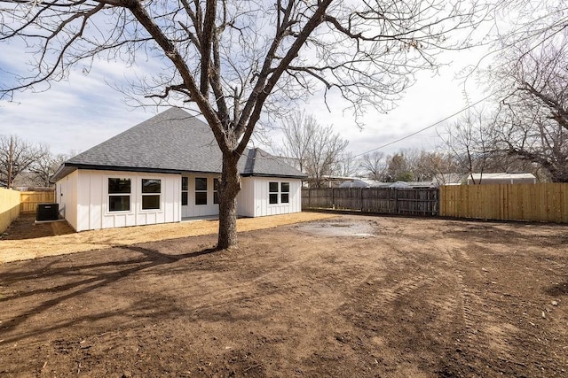 rear view of house featuring a shingled roof, board and batten siding, a fenced backyard, and central air condition unit