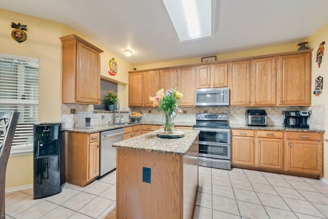 kitchen with light tile patterned floors, tasteful backsplash, appliances with stainless steel finishes, light stone counters, and a center island