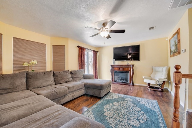 living area with ceiling fan, visible vents, wood finished floors, and a glass covered fireplace