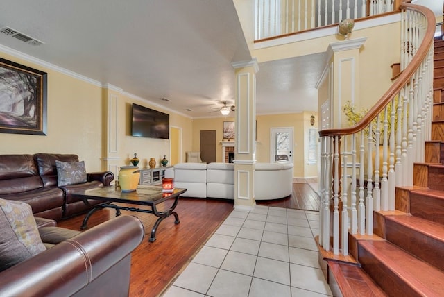 living area with crown molding, visible vents, a ceiling fan, ornate columns, and stairs