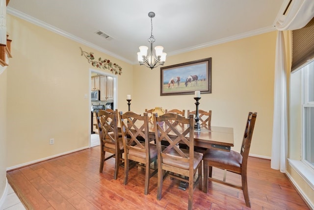 dining area featuring visible vents, light wood-style flooring, an inviting chandelier, ornamental molding, and baseboards