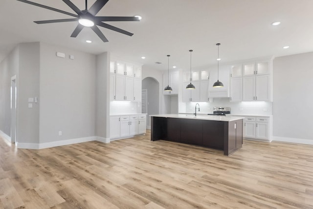 kitchen with arched walkways, light countertops, light wood-style floors, white cabinets, and stainless steel range with electric stovetop