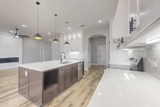 kitchen with tasteful backsplash, arched walkways, light wood-style flooring, appliances with stainless steel finishes, and a sink