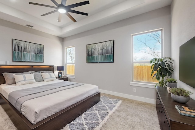 bedroom featuring light carpet, baseboards, visible vents, a raised ceiling, and a ceiling fan