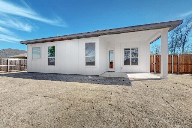 rear view of property featuring board and batten siding, a fenced backyard, and a patio