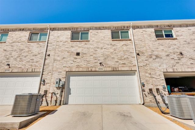 view of front of home featuring a garage, driveway, cooling unit, and brick siding