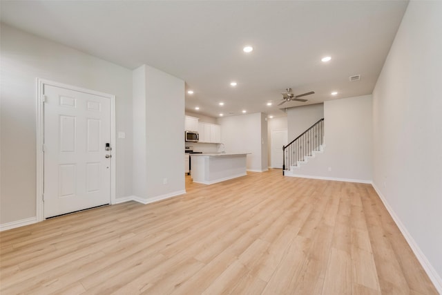 unfurnished living room featuring recessed lighting, light wood-style flooring, ceiling fan, baseboards, and stairs