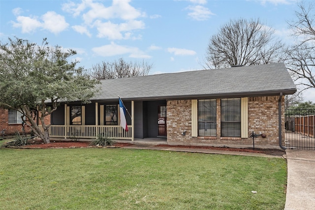 view of front of house featuring brick siding, fence, a front yard, roof with shingles, and covered porch