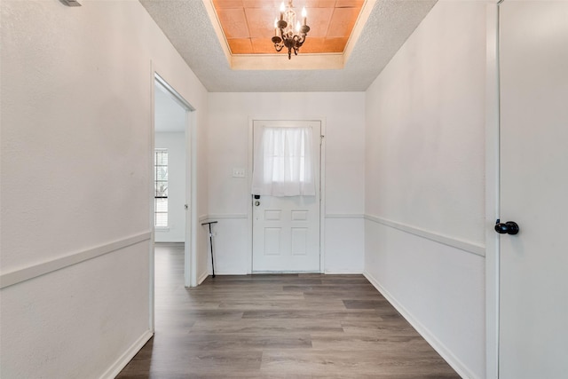 doorway with a raised ceiling, wood finished floors, baseboards, and a textured ceiling