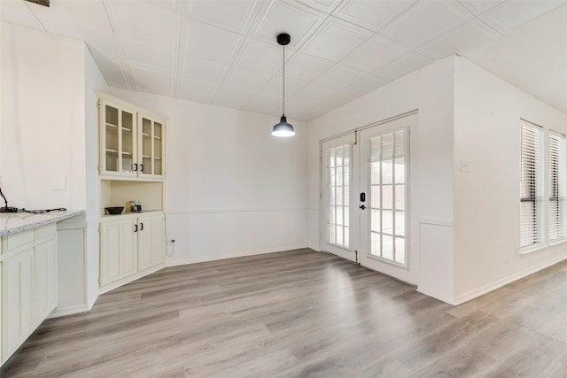 unfurnished dining area featuring french doors, baseboards, and light wood-style floors