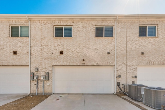 back of property featuring a garage, cooling unit, concrete driveway, and brick siding