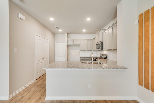 kitchen with a peninsula, light stone counters, stainless steel appliances, and a sink