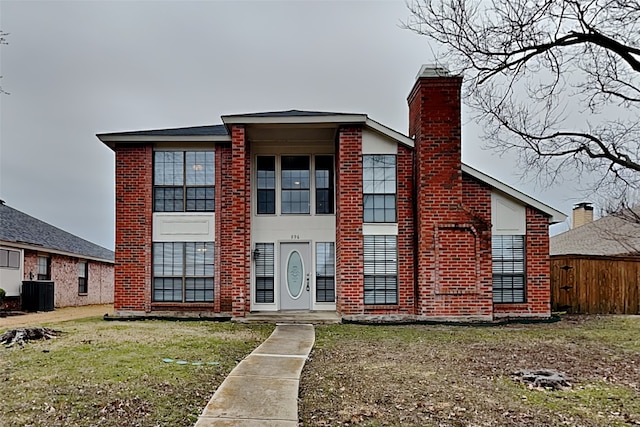 view of front facade with central AC unit, a chimney, fence, a front lawn, and brick siding