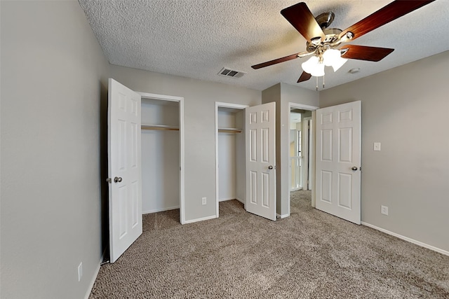 unfurnished bedroom with a textured ceiling, carpet floors, visible vents, baseboards, and multiple closets