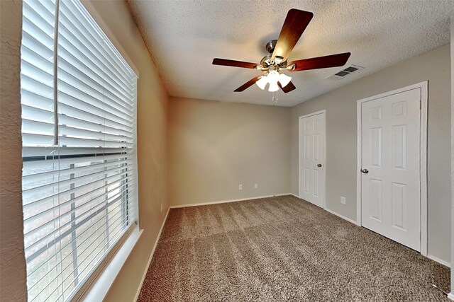 empty room featuring a textured ceiling, carpet floors, a wealth of natural light, and visible vents