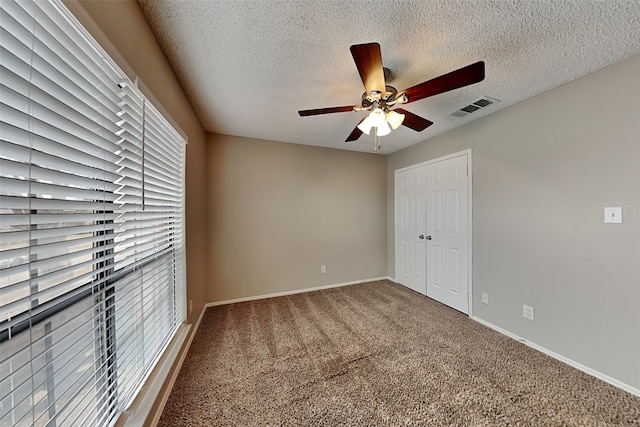 unfurnished bedroom with visible vents, baseboards, carpet, a textured ceiling, and a closet