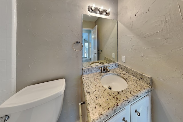 bathroom with a textured wall, vanity, and toilet