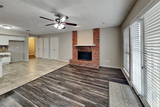 unfurnished living room with light wood-style flooring, a fireplace, ceiling fan, and a textured ceiling