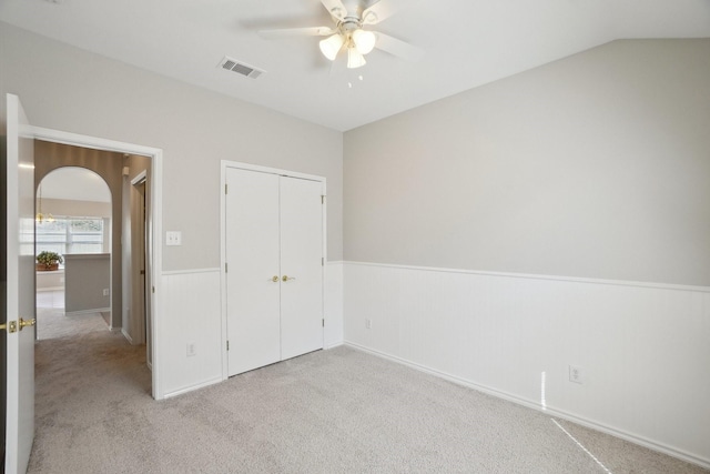 unfurnished bedroom with arched walkways, a closet, visible vents, wainscoting, and carpet flooring