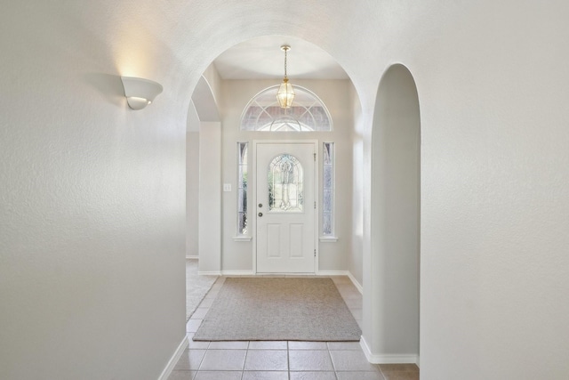 entryway with arched walkways, light tile patterned flooring, and baseboards