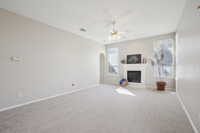 unfurnished living room featuring arched walkways, visible vents, a glass covered fireplace, and baseboards