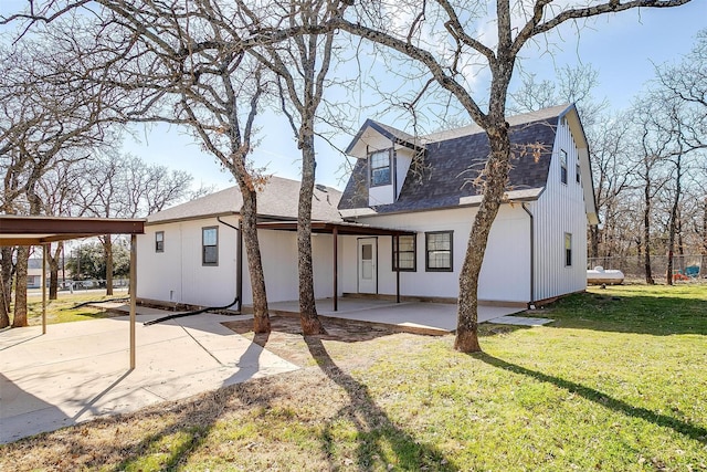 back of house with a lawn, a patio, a gambrel roof, roof with shingles, and a carport