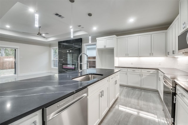 kitchen with a sink, white cabinetry, appliances with stainless steel finishes, stainless steel counters, and a tray ceiling