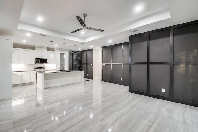 kitchen featuring a tray ceiling, stainless steel microwave, a decorative wall, and white cabinetry