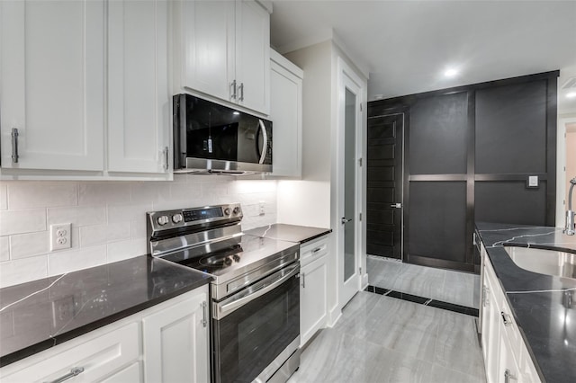 kitchen with tasteful backsplash, white cabinetry, stainless steel appliances, and dark stone counters