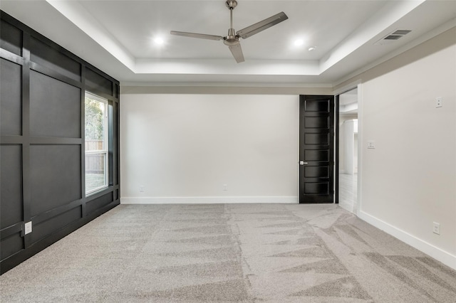 carpeted empty room featuring baseboards, visible vents, a tray ceiling, and ceiling fan