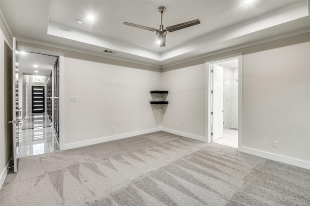 spare room featuring carpet, a tray ceiling, visible vents, ceiling fan, and baseboards