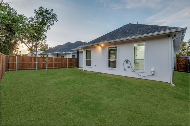 rear view of property with a yard, a shingled roof, a fenced backyard, and stucco siding