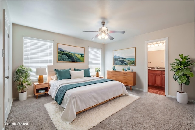 bedroom featuring ceiling fan, ensuite bathroom, light carpet, a sink, and baseboards