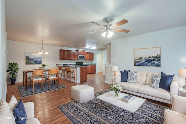 living area with ceiling fan with notable chandelier, light wood-style flooring, and baseboards