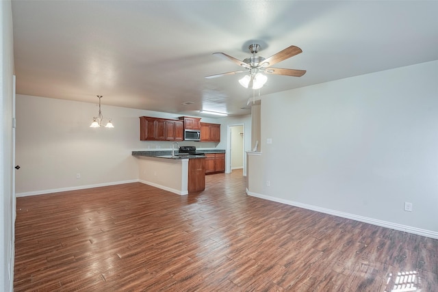 kitchen with a peninsula, open floor plan, dark wood-style floors, stainless steel microwave, and dark countertops