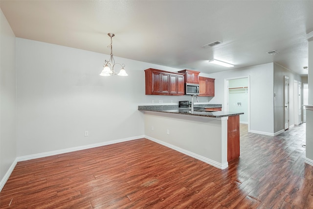 kitchen with baseboards, visible vents, stainless steel microwave, dark wood-type flooring, and a peninsula