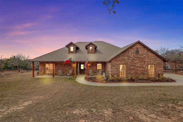 view of front of house with brick siding, a front lawn, fence, roof with shingles, and a patio