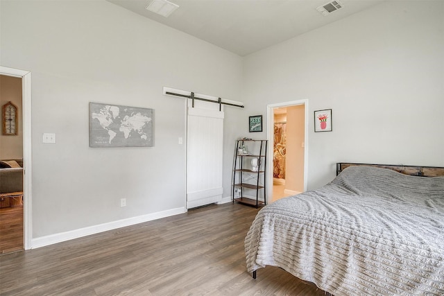 bedroom with wood finished floors, visible vents, baseboards, and a barn door