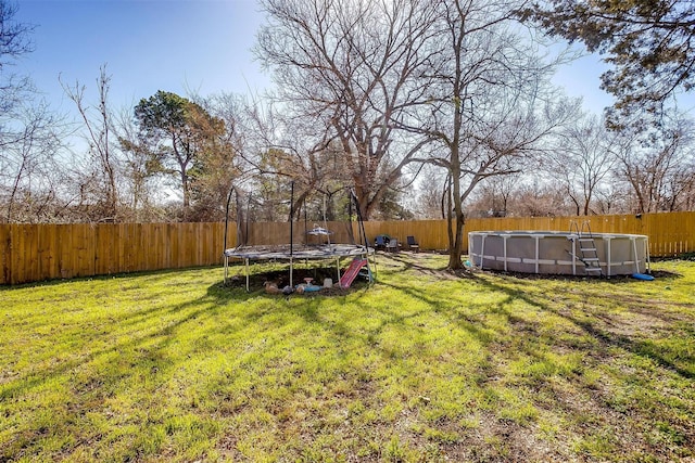 view of yard with a trampoline, a fenced backyard, and a fenced in pool