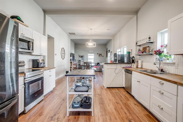 kitchen featuring light wood-style flooring, a sink, stainless steel appliances, open shelves, and wooden counters