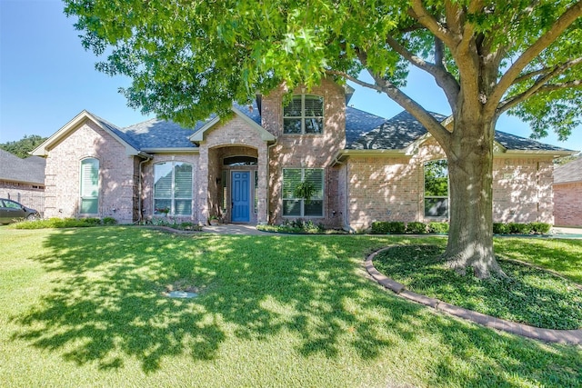 view of front of house featuring a shingled roof, brick siding, and a front lawn