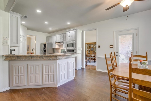 kitchen with a peninsula, stainless steel microwave, dark wood finished floors, and visible vents