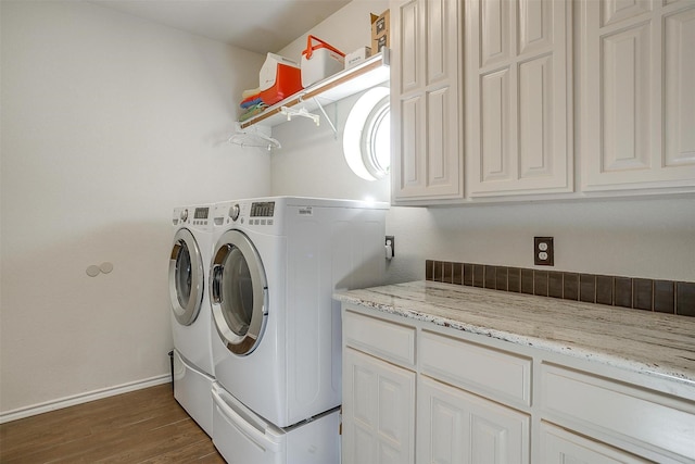 washroom with dark wood-style flooring, washer and clothes dryer, cabinet space, and baseboards